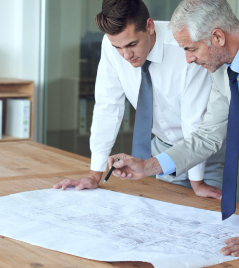 Two business professionals in formal attire analyzing a blueprint together, focused on their collaborative work.